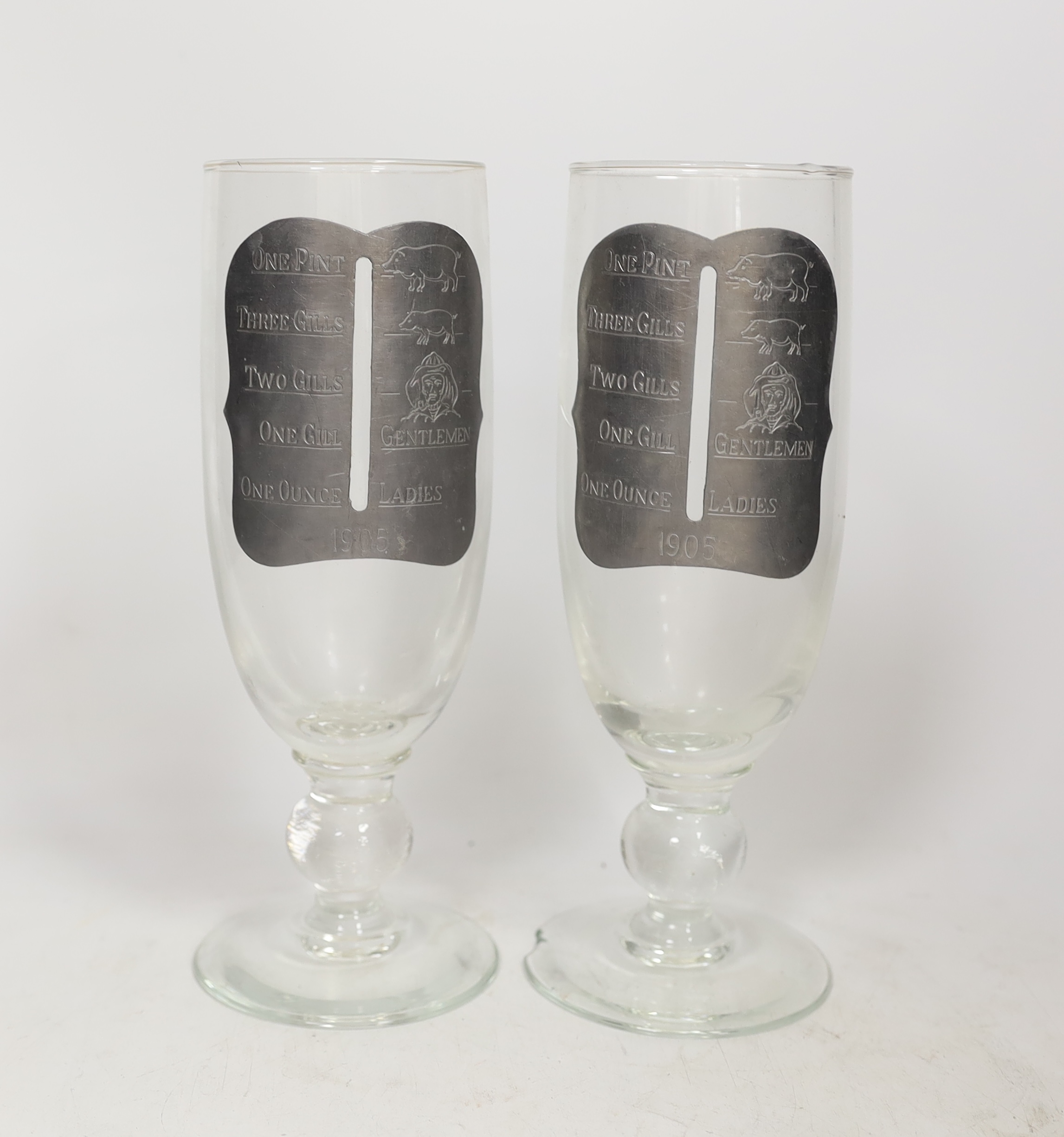 A pair of early 20th century drinking glasses with pewter measures, in a wooden case, one cracked and chipped, 24cm